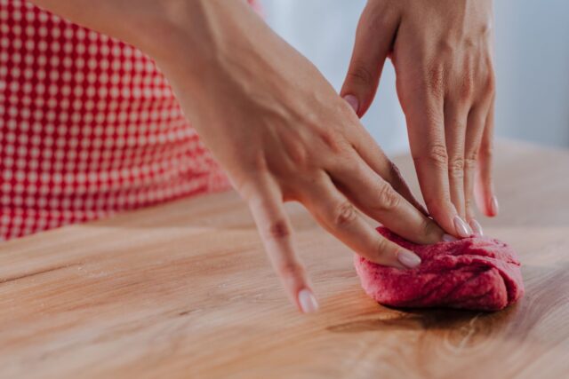 Mâini care frământă aluat pentru paste proaspete pe o masă de lemn, într-un atelier de gătit